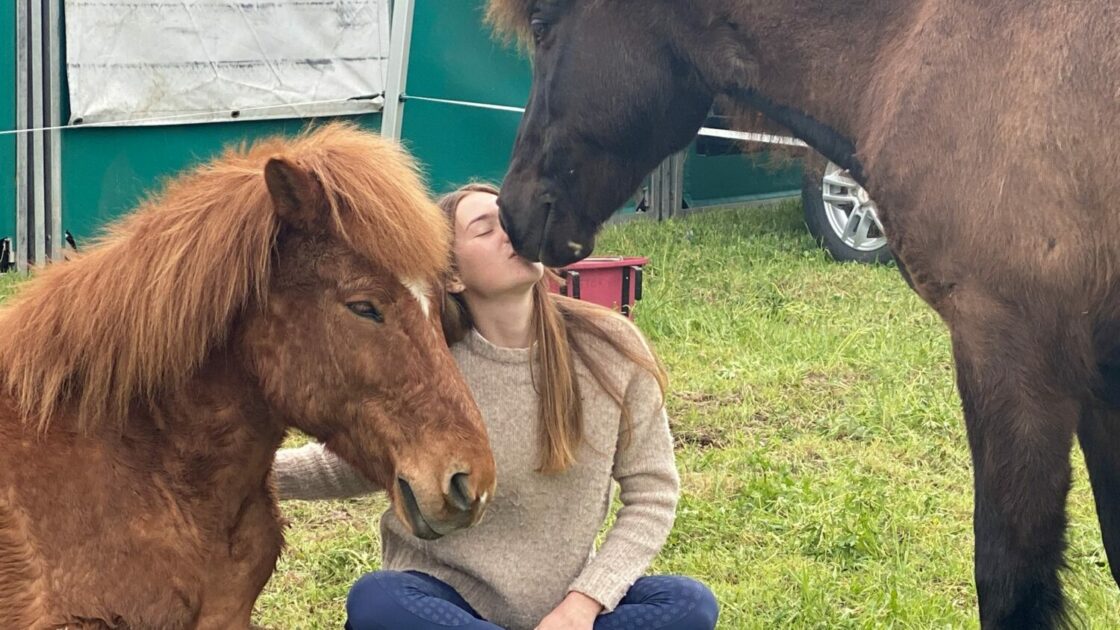 Lorraine Essl sitzt am Boden und ist umringt von ihren Pferden